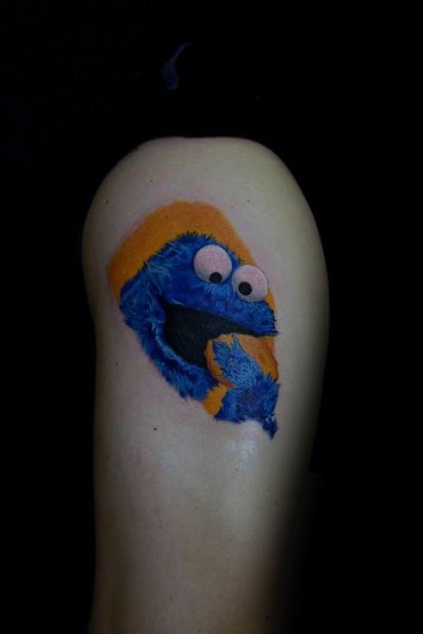 Small Cookie Monster tattoo on the back of the arm, featuring a cheerful expression with a cookie and bold orange background.