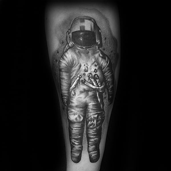 Realistic black and grey Deja Entendu astronaut tattoo with deep shading and space-like background details on the forearm.