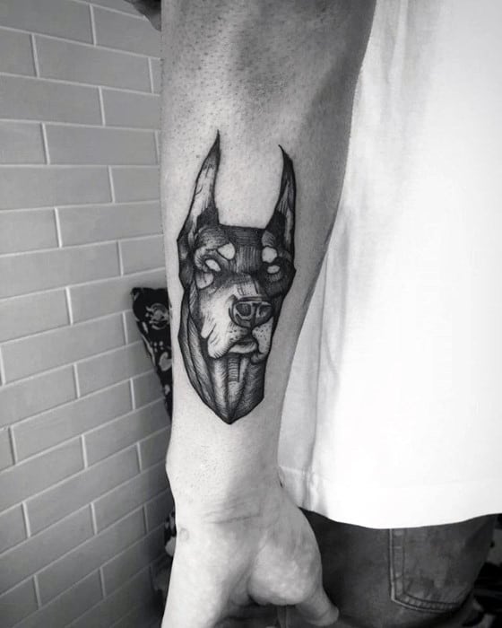Minimalist black and grey Doberman tattoo with fine lines, hollow eyes, and a sharp-edged design placed on the inner forearm.
