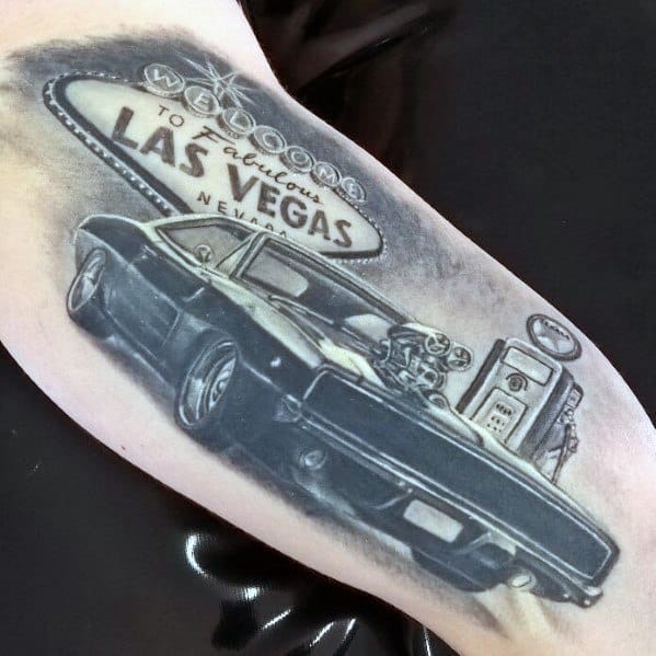 Black and grey Dodge Charger tattoo with a supercharger, Las Vegas sign, and gas pump, creating a bold muscle car and cityscape design.
