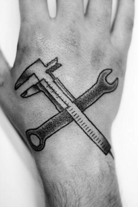 Tattoo of a caliper and wrench crossed in an X shape on the hand, symbolizing precision, craftsmanship, and mechanical skill.