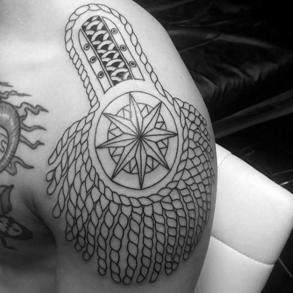 Outline-style epaulette tattoo with a compass rose centerpiece and cascading rope-like tassels draping over the shoulder.