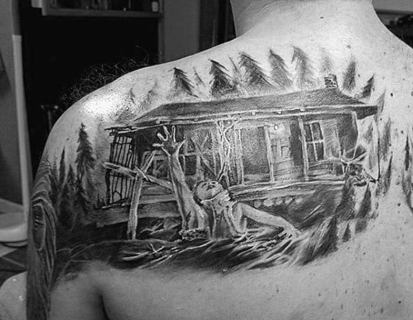 Black and grey Evil Dead shoulder tattoo of a woman reaching out from the ground in front of the haunted cabin surrounded by eerie forest trees