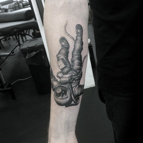Detailed tattoo of an astronaut floating or falling in space, inked on the forearm with a realistic spacesuit and tether line.
