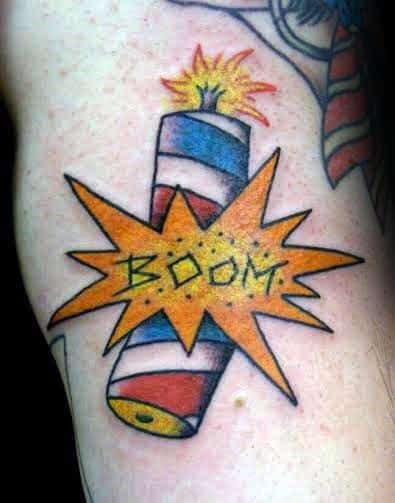 Tattoo of a firecracker wrapped in red, white, and blue with a lit fuse, exploding with a bold "BOOM" in a comic-style burst.