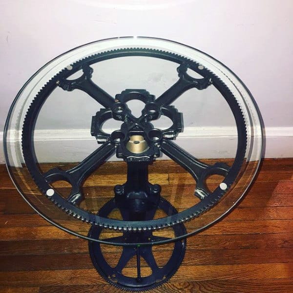 A round glass table with a bicycle gear and chain mechanism as its base on a wooden floor