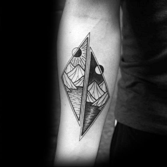 Geometric forearm tattoo with split diamond shape showing mountain and sea landscapes in day and night scenes.