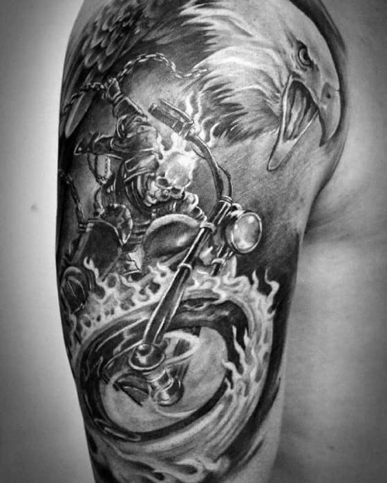 Black and grey Ghost Rider upper arm tattoo with a flaming motorcycle, fierce eagle, and dynamic motion lines for a powerful look.