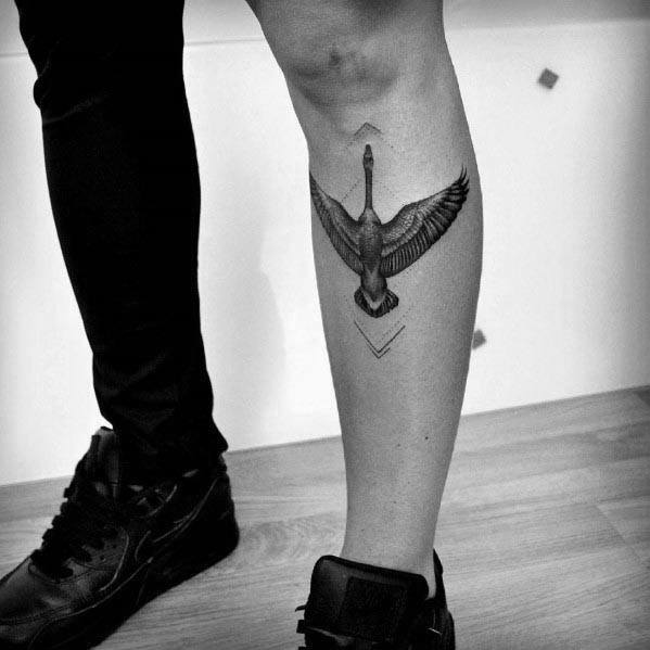 Black and gray tattoo of a goose flying upward with outstretched wings, inked on the calf with fine shading and geometric accents.