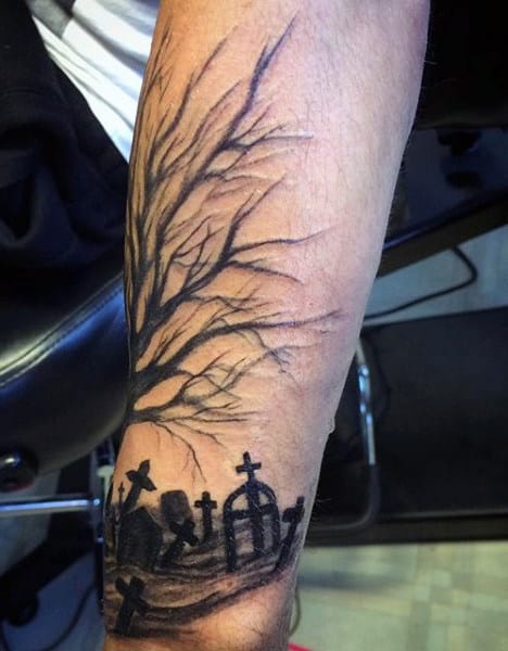 Tattoo of a haunting graveyard with crosses and a leafless tree on a person's forearm