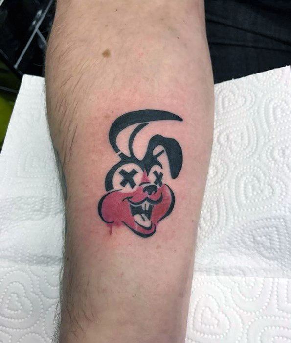 Tattoo of a pink-cheeked cartoon bunny with X eyes and a mischievous grin, inspired by Green Day’s punk mascot style.