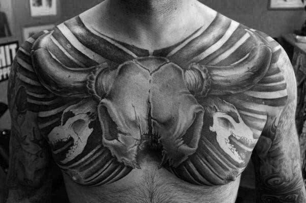 A black and white chest tattoo featuring a bull skull and other skull designs