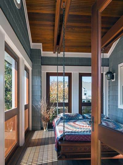 Hanging bed with chains, patterned bedding, and wooden ceiling in a cozy sunroom.