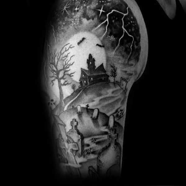 Upper arm tattoo of a haunted church on a hill with gravestones, lightning, bats, bare trees, and a glowing full moon in the night sky.