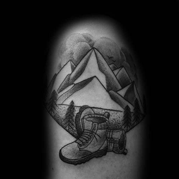 A black and gray tattoo of mountains with pine trees, a hiking boot, and a backpack, symbolizing outdoor adventure and exploration.