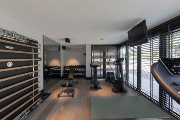 Modern home gym featuring exercise equipment like weights, bikes, and treadmill, surrounded by windows