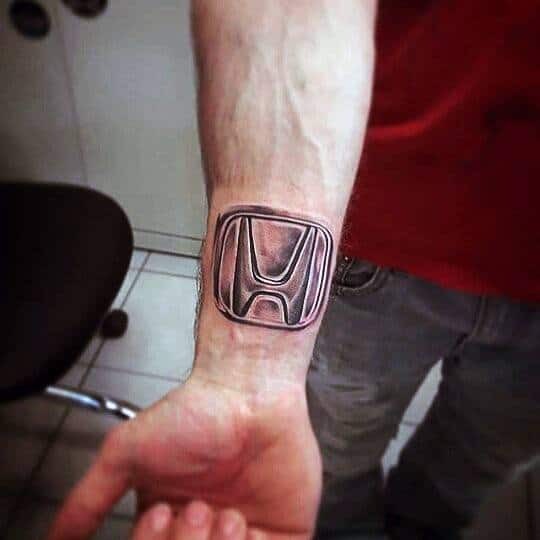Realistic Honda logo tattoo on a man's wrist, featuring bold shading and a three-dimensional metallic effect for a striking look.