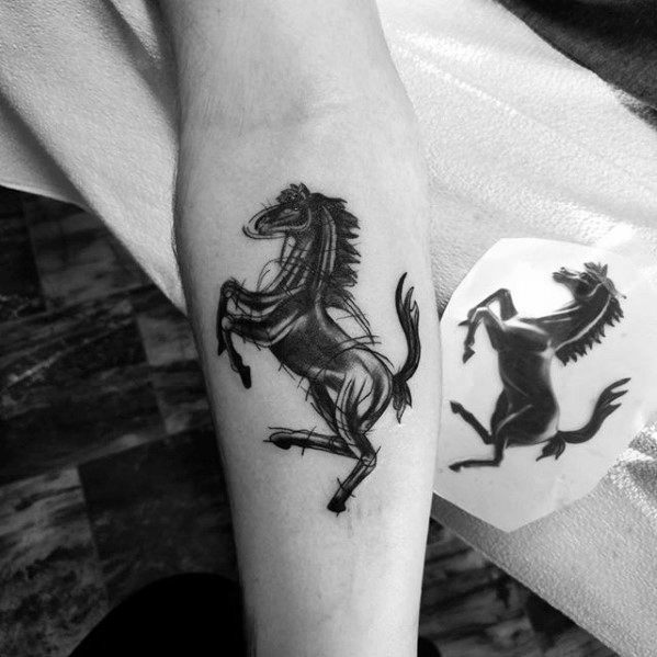 Black ink tattoo of a rearing horse on the forearm, inspired by the Ferrari logo, with bold lines and a dynamic pose