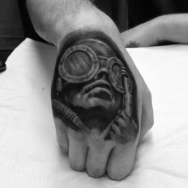 HR Giger-inspired hand tattoo featuring a surreal figure wearing large goggles, with biomechanical tubing and dark, shadowed detailing.