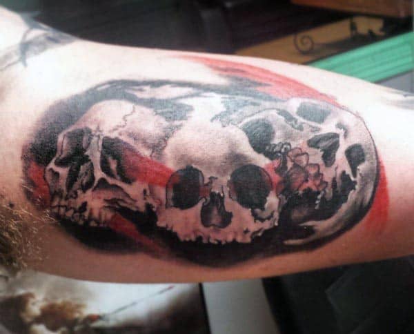 Dark and bold tattoo of multiple skulls in a circular design, accented with red streaks, creating a haunting and dramatic look on the bicep