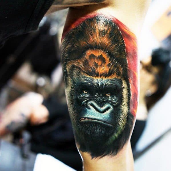 Vivid color King Kong tattoo on upper arm featuring a calm yet intense expression, with realistic fur texture and a fiery red-orange background.
