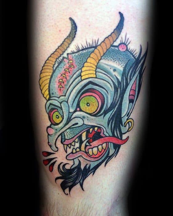 Colorful Krampus tattoo with a grotesque horned head, bulging yellow eyes, stitched forehead, gold earring, and blood dripping from sharp teeth.