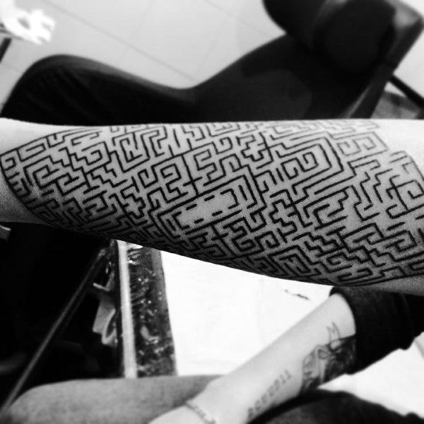 Intricate black ink labyrinth tattoo covering a man's forearm, featuring a detailed maze pattern with fine lines and geometric precision.