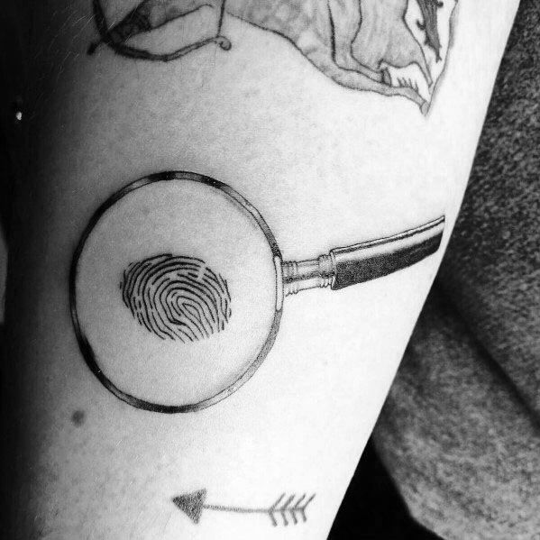 Minimalist tattoo of a magnifying glass focusing on a fingerprint, symbolizing identity and detail, with clean black ink lines for a sleek design.