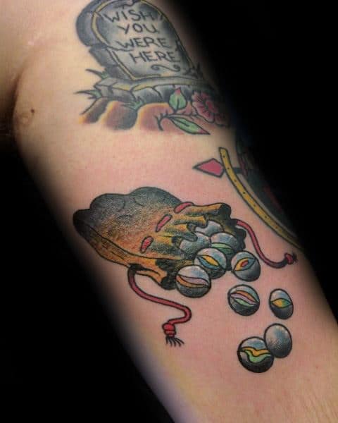 Colorful tattoo of a worn drawstring bag spilling marbles, symbolizing childhood memories, with bold shading and vibrant details for a nostalgic look.