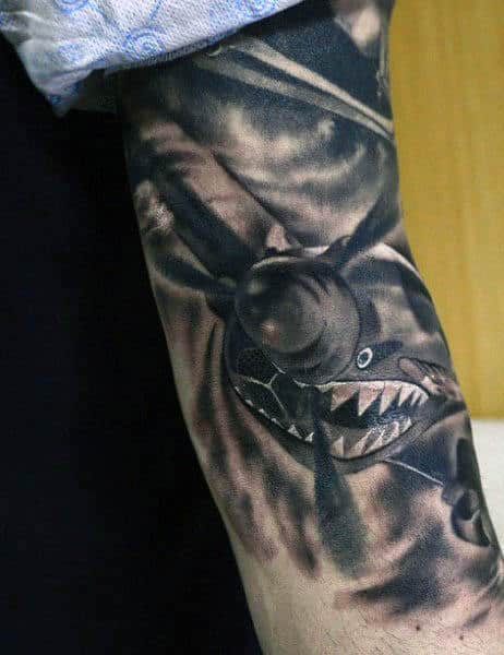 Tattoo of a fighter airplane with a shark face on a person's arm