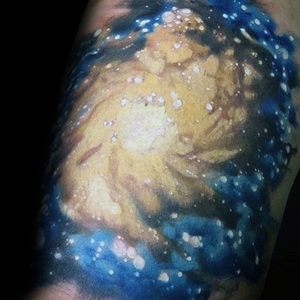 Tattoo of a swirling galaxy with golden clouds and blue accents, reminiscent of a nebula on a dark background