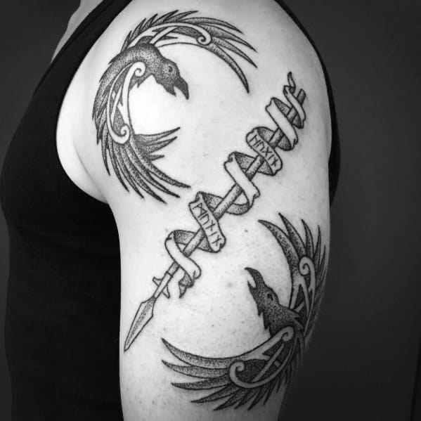 Dotwork tattoo of Huginn and Muninn circling a rune-wrapped spear, inked on the upper arm with bold Norse-inspired curves.
