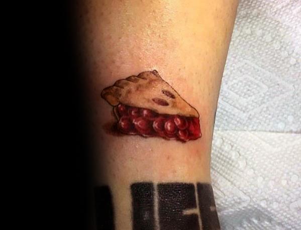 Small and realistic cherry pie slice tattoo with a golden crust and juicy filling, creating a subtle yet detailed dessert-inspired design