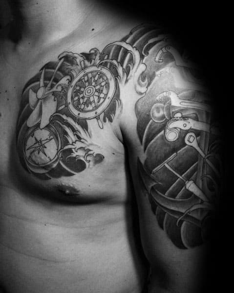 Black and grey chest and shoulder tattoo featuring a ship’s wheel, propeller, and nautical elements with bold shading and wave-like details.