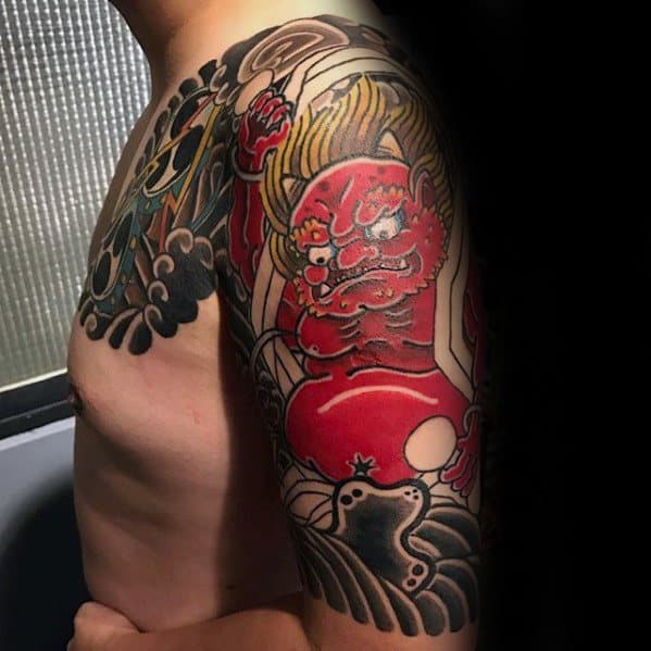 Raijin upper arm tattoo with a bold red thunder god, raised fist, flowing hair, and dramatic black cloud patterns in Japanese style.
