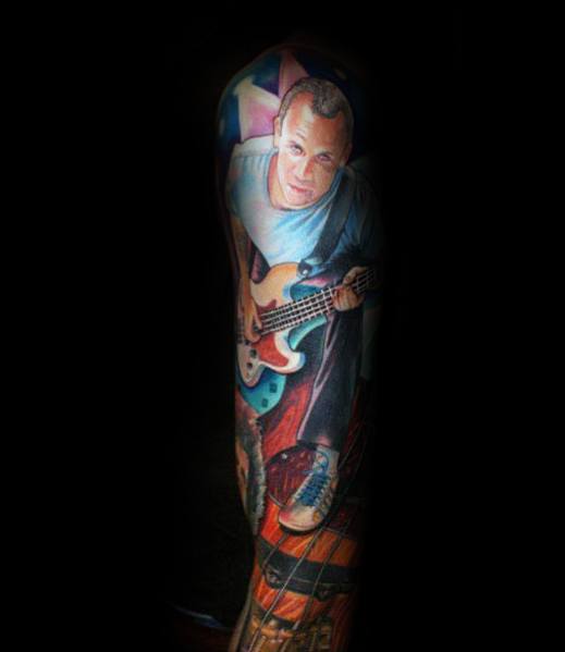 Full sleeve tattoo featuring a realistic, vibrant portrait of a bass guitarist mid-performance, with dynamic lighting and bold colors for a lifelike effect.