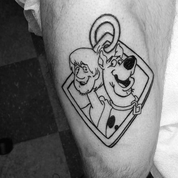 Black and white tattoo of Shaggy and Scooby-Doo inside a dog tag-shaped frame, both smiling with a playful expression.