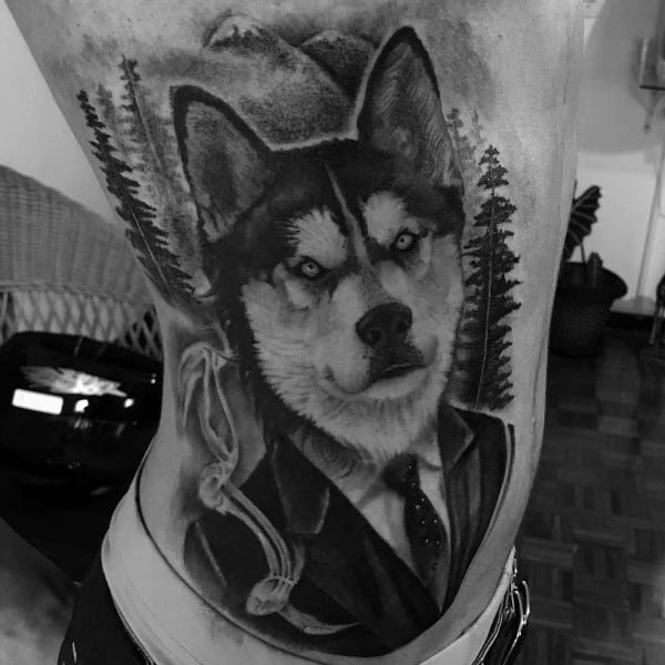 Black and gray Siberian Husky tattoo on a man's ribs, featuring the dog in a suit with a forest background for a unique and artistic design.