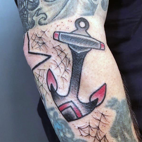 Traditional black anchor tattoo with red accents, bold shading, and spider web details, creating a nautical and edgy design on the arm.