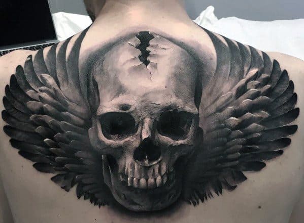 Realistic skull back tattoo with cracked crown and detailed black wings spreading across the shoulder blades for a powerful, dark look.