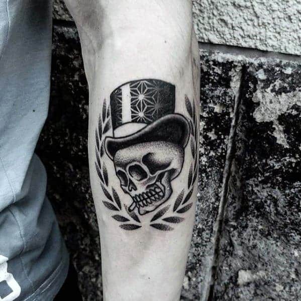Tattoo of a skull wearing a top hat with a laurel wreath on a person's arm
