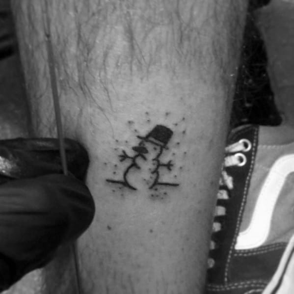 Minimalist snowman tattoo in a simple black ink design, featuring a tiny snowman with a top hat and twig arms, creating a subtle winter charm.
