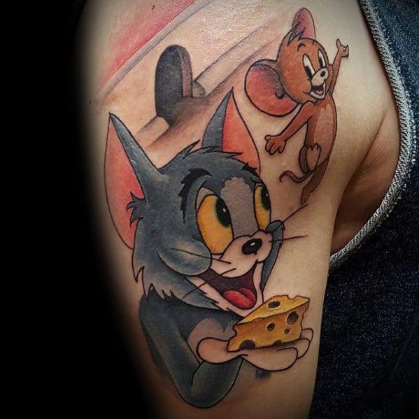 Vibrant upper arm tattoo of Tom holding cheese and looking up at a playful Jerry escaping through a mouse hole.