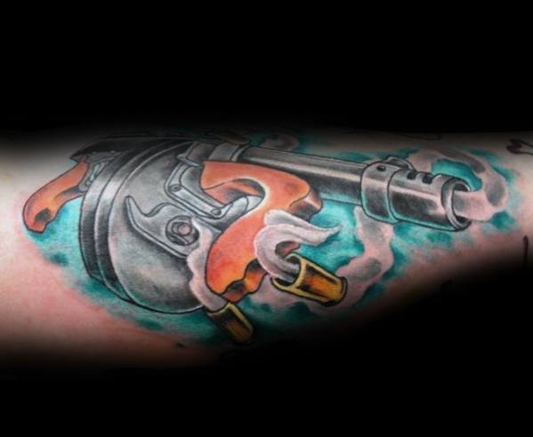 Dynamic Tommy gun tattoo with bold colors, smoke effects, and flying bullet casings, creating a striking and action-packed design on the forearm.
