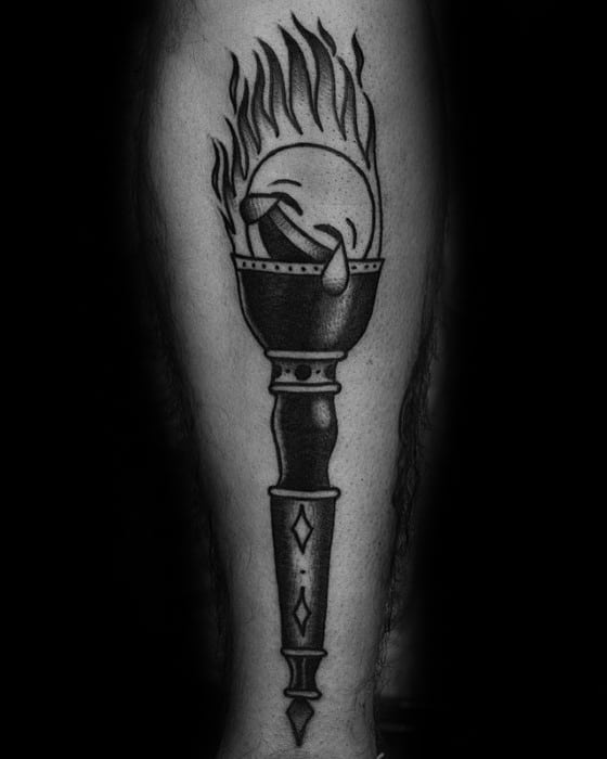 Blackwork torch tattoo with a crying smiley face engulfed in flames, set atop a textured handle with diamond details.
