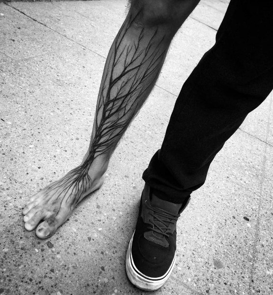 Black ink leg tattoo of intricate tree branches extending from the foot up the calf, blending seamlessly with the body's natural form for an organic look.