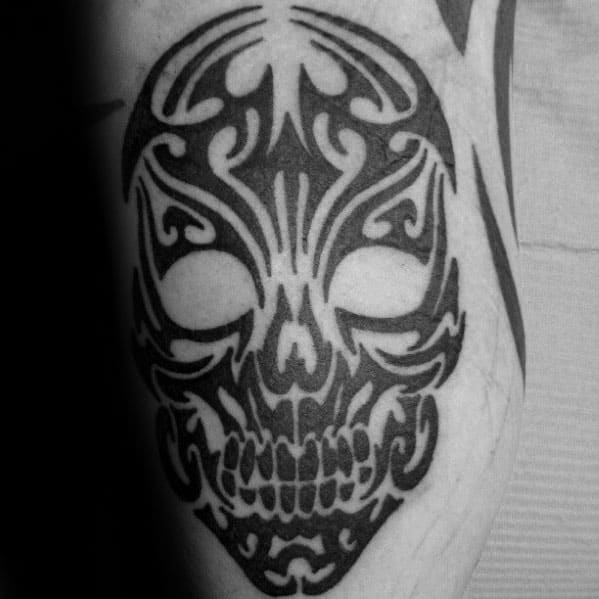 Symmetrical tribal skull tattoo with bold black ink, featuring flowing patterns and hollow eyes for a clean yet fierce forearm design.