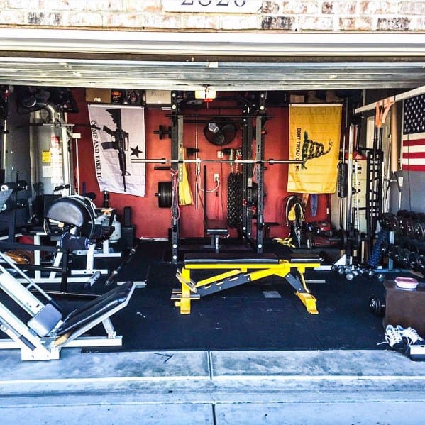 Two-car garage gym with squat rack, weight bench, flags, and compact fitness equipment setup.