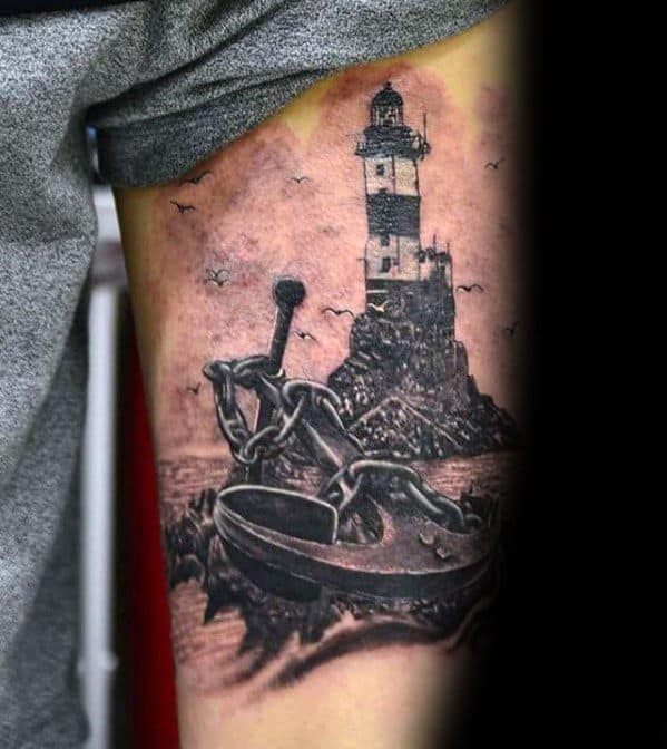 Tattoo of an anchor with a chain and lighthouse in the background on an arm