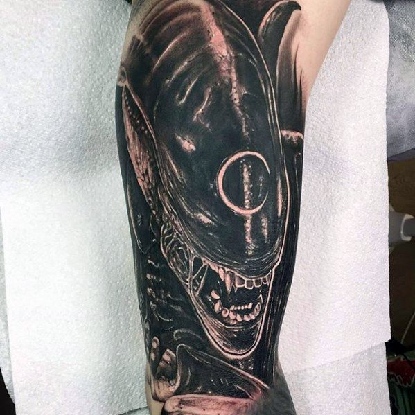 High-contrast Xenomorph tattoo on arm with detailed shading, fierce expression, and circular mark on the creature’s head.